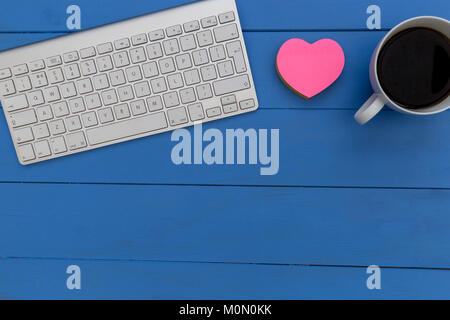 Wireless computer keyboard coffee and love heart on blue wood desk workspace Stock Photo