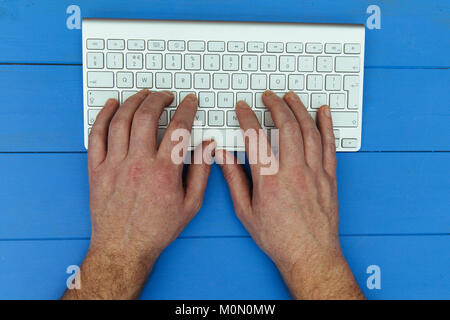 Man typing on wireless computer keyboard on blue wood desk background Stock Photo