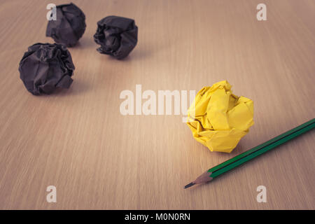 Business Creative and Idea Concept : Used pencil with yellow crumpled paper ball put on wooden foor and black crumpled paper ball in the background. Stock Photo