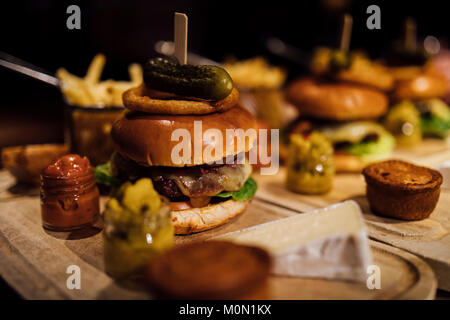 Close up shot of a restaurant burger meal with onion rings, bacon, pickle, chips and garnishes. Stock Photo