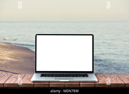 Modern laptop with empty white screen on wooden table against blurred beach background Stock Photo