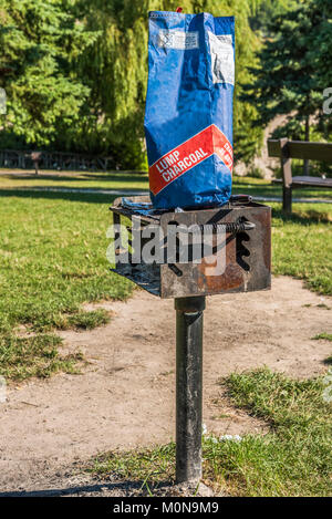 A bag of charcoal sits on a rusty metal barbecue spit in a picnic area of a park. Stock Photo
