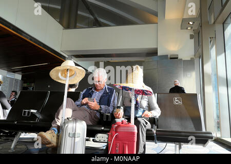 A senior couple going on holiday with luggage & straw hats sitting inside  departure lounge at LAX airport Los Angeles, California USA    KATHY DEWITT Stock Photo