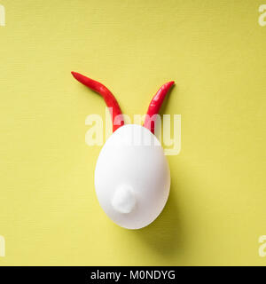 Egg shell and red hot chilli pepper imitation rabbit hare face of devil clown on yellow colored background paper. Food concept minimal Easter Hallowee Stock Photo