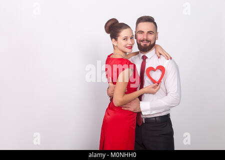 Young couple celebrate valentines day, hugging and toothy smile. Indoor, studio shot, isolated on gray background Stock Photo