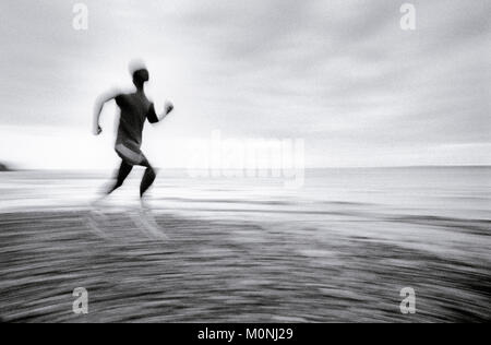 A blurred panning shot of a man running on beach, profile (distorted) Stock Photo