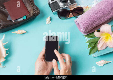 Travel concept, sunglasses and summer accessories on blue background. Smartphone in female hands. View from above. Blank mock up for advertising or pa Stock Photo