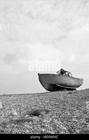 Old wrecked wooden shiplap fishing boat washed up on pebbles at Dungeness Kent coast.Old wrecked boat on beech