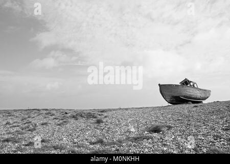 Old wrecked wooden shiplap fishing boat washed up on pebbles at Dungeness Kent coast.Old wrecked boat on beech Stock Photo