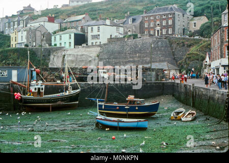 Low tide in the harbour at Fowey, Cornwall in 1981. People walking along the quayside, two large trawlers and three smaller boats rest on the seabed. Seagulls scavenge for food on the sea floor. Stock Photo