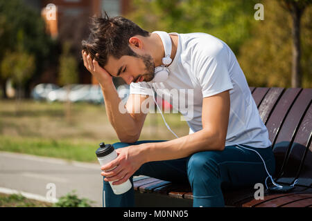 Young man is relaxing and drinking water after jogging. Stock Photo