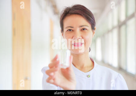 Smiling female nurse holding pill cup in her hands for patients. Professional, Specialist, Nurse, Doctor in white uniform concept. Stock Photo