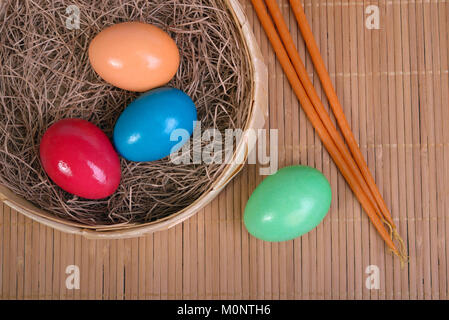 Multicolored eggs in the straw in a basket and candles on a mat next Stock Photo