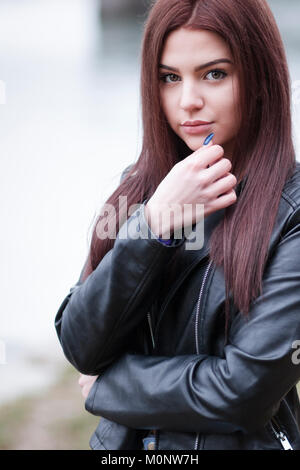 Thoughtful attractive young brunette woman standing outdoors with her hand to her chin staring intently at the camera with a calm expression Stock Photo