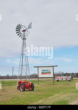 Roadside signs, a red tractor and a windmill water pump advertise a Farm Market in rural Pike Road Alabama, United States. Stock Photo