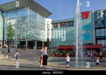 France,Puy de Dome,Clermont Ferrand,Place of Jaude,children with their parents at the foot of a water jet with a shopping mall in the background Stock Photo