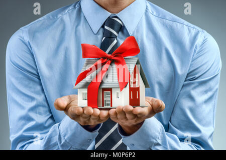 Worker in blue shirt holding house with red ribbon. Close up. Business concept Stock Photo