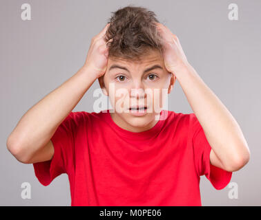 Emotional portrait of excited teen boy. Funny cute surprised child 14 year old with mouth open in amazement. Shocked teenager with hands on head, on g Stock Photo