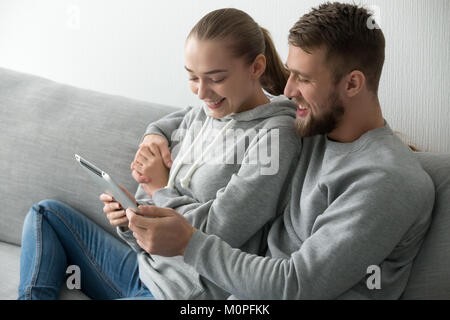 Smiling couple embracing using tablet together on couch at home