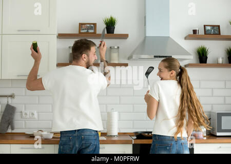 Funny couple having fun cooking in kitchen together, rear view Stock Photo