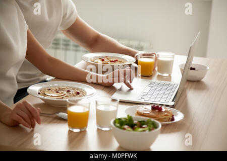 Couple having breakfast using laptop on dining table, close up Stock Photo