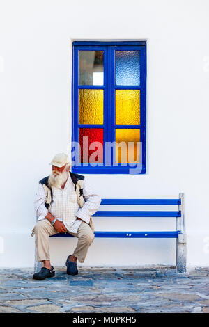 Portrait of an old man smoking seated on a blue bench in Mikonos, Greece Stock Photo