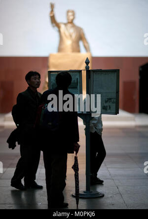 North Korean people reading a newspaper in Kaeson metro station in front of a golden statue of Kim il Sung, Pyongan Province, Pyongyang, North Korea Stock Photo