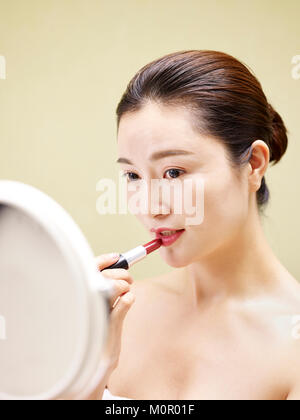 beautiful young asian woman looking in the mirror while applying lipstick on lips. Stock Photo