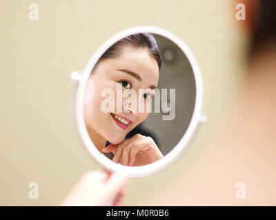beautiful young asian woman looking at self in mirror, happy and smiling.