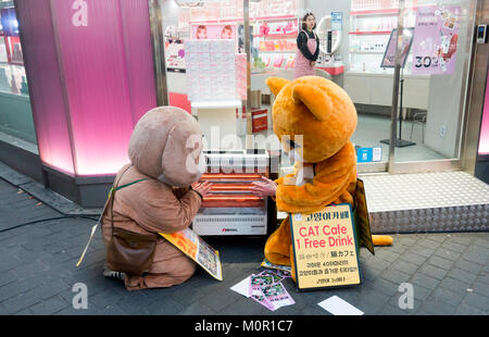 Seoul, South Korea. 23rd January, 2018. Korean weather, Jan 23, 2018 : Part-time workers promoting pet cafes get warm by an electric heater of a cosmetics store on Myeongdong shopping street in Seoul, South Korea. An extreme cold wave hit the country on Tuesday with lows of minus 13 degrees Celsius and with wind chill temperature of minus 20.1 C in Seoul, according to the Korean Meteorological Administration. Credit: Lee Jae-Won/AFLO/Alamy Live News Stock Photo