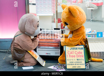 Seoul, South Korea. 23rd January, 2018. Korean weather, Jan 23, 2018 : Part-time workers promoting pet cafes get warm by an electric heater of a cosmetics store on Myeongdong shopping street in Seoul, South Korea. An extreme cold wave hit the country on Tuesday with lows of minus 13 degrees Celsius and with wind chill temperature of minus 20.1 C in Seoul, according to the Korean Meteorological Administration. Credit: Lee Jae-Won/AFLO/Alamy Live News Stock Photo