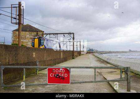 Saltcoats, Scotland, UK. 24th January  2018. UK Weather: A train passing through Saltcoats travels next to the coastline as high winds cause waves to crash against the sea wall. The road is closed for safety reasons. Storm Georgina is the seventh named storm of the season and is forecast to bring high wind and rain sweeping easterly across Britain. Credit: Skully/Alamy Live News Stock Photo