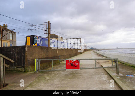 Saltcoats, Scotland, UK. 24th January  2018. UK Weather: A train passing through Saltcoats travels next to the coastline as high winds cause waves to crash against the sea wall. The road is closed for safety reasons. Storm Georgina is the seventh named storm of the season and is forecast to bring high wind and rain sweeping easterly across Britain.. Credit: Skully/Alamy Live News Stock Photo