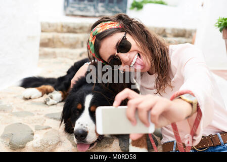 Brunette girl taking selfie of a cute bernese mountain dog lying on the floor tired and her. Stock Photo