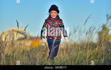 Laughing Happy little girl running in sunlight on autumn meadow. Stock Photo