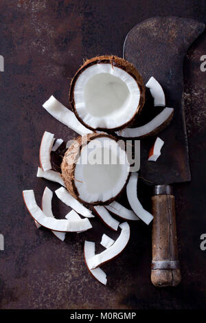 Opened coconut, cocontu pieces and an old cleaver Stock Photo