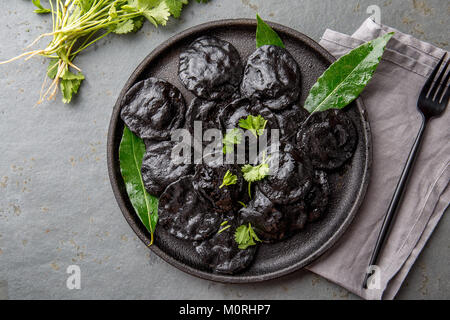 Traditional Italian black ravioli on black plate, gray stone slate background. Top view. Stock Photo