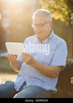 Outdoor portrait of happy senior man who is using digital tablet. Stock Photo