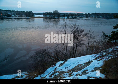 Lake view with frozen waters taken from a rocky shore. On the other side of the lake there are forests and some farm lands. Stock Photo