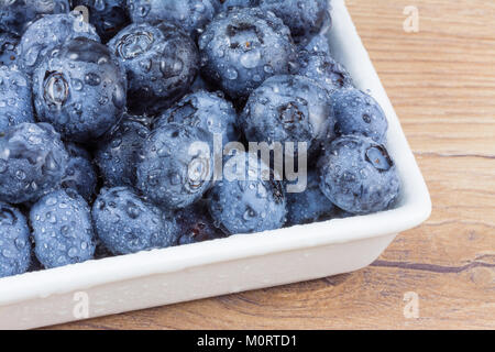 Fresh bilberries with drops of water. Close-up of forest blueberries in a white bowl on wooden table. Stock Photo