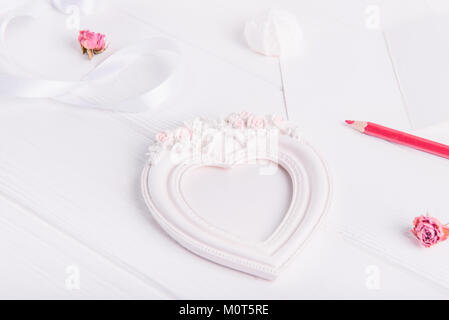 Heart shaped photo frame with clipping path of the gypsum, red pencil, greeting card on the white wooden table. Gifts for Valentine's Day for a loved one. Selective focus. Stock Photo