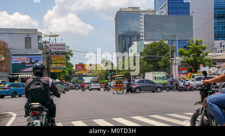 A woman pushes a foodcart down the middle of the street at a busy intersection. Semarang, Java, Indonesia. Stock Photo