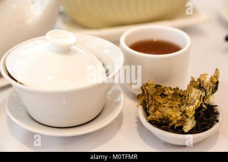 Brewing Chinese tea for dim sum meal with tea leaves and traditional tea cup in the foreground. Stock Photo