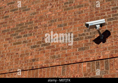 The image shows a CCTV camera mounted on a brick wall, often used for surveillance purposes in urban environments. It represents modern security technologies in public and private spaces. Stock Photo