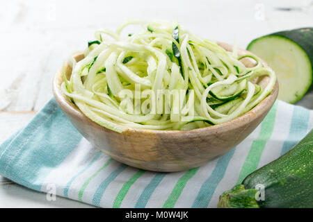 Raw zucchini spaghetti in a rustic wooden bowl on white table Stock Photo