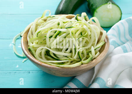 Raw zucchini spaghetti in a rustic wooden bowl on a turquoise wooden table Stock Photo