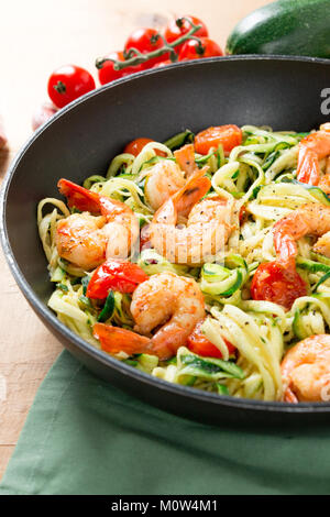 Zucchini spaghetti sauteed with tomato cherry and prawns in a pan on a rustic wooden table. Close up Stock Photo