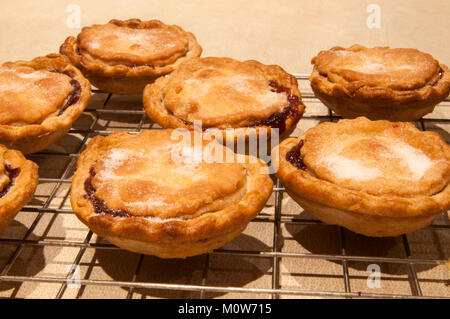 Freshly cooked homemade Mince pies, hot out of the oven and cooling down on a wire rack, with a sprinkling of sugar. A traditional Christmas treat. Stock Photo