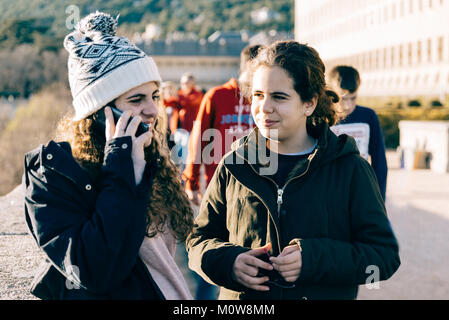 Happy teenage girls on of them in knit hat texting with cell phone in landmark. Concept togetherness Stock Photo