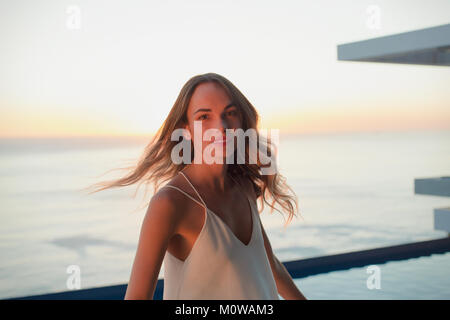 Portrait confident woman turning on luxury balcony with sunset ocean view Stock Photo